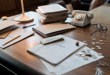 Documentos financeiros, moedas, óculos e um telefone antigo sobre uma mesa de escritório.