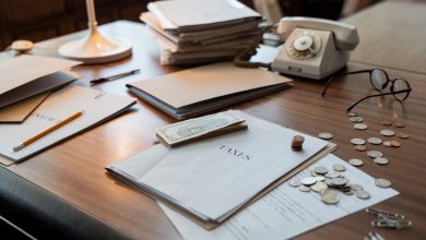 Documentos financeiros, moedas, óculos e um telefone antigo sobre uma mesa de escritório.
