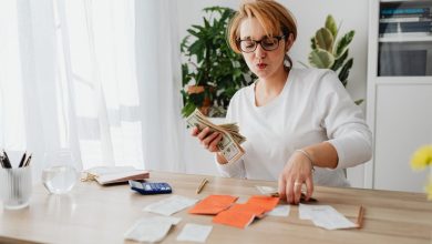 Pessoa contando dinheiro e organizando recibos sobre uma mesa, com uma calculadora ao lado.