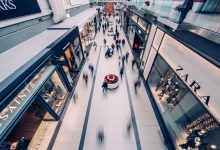 Shopping movimentado, com consumidores circulando diante de lojas modernas.