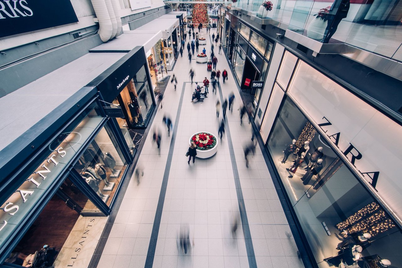 Shopping movimentado, com consumidores circulando diante de lojas modernas.